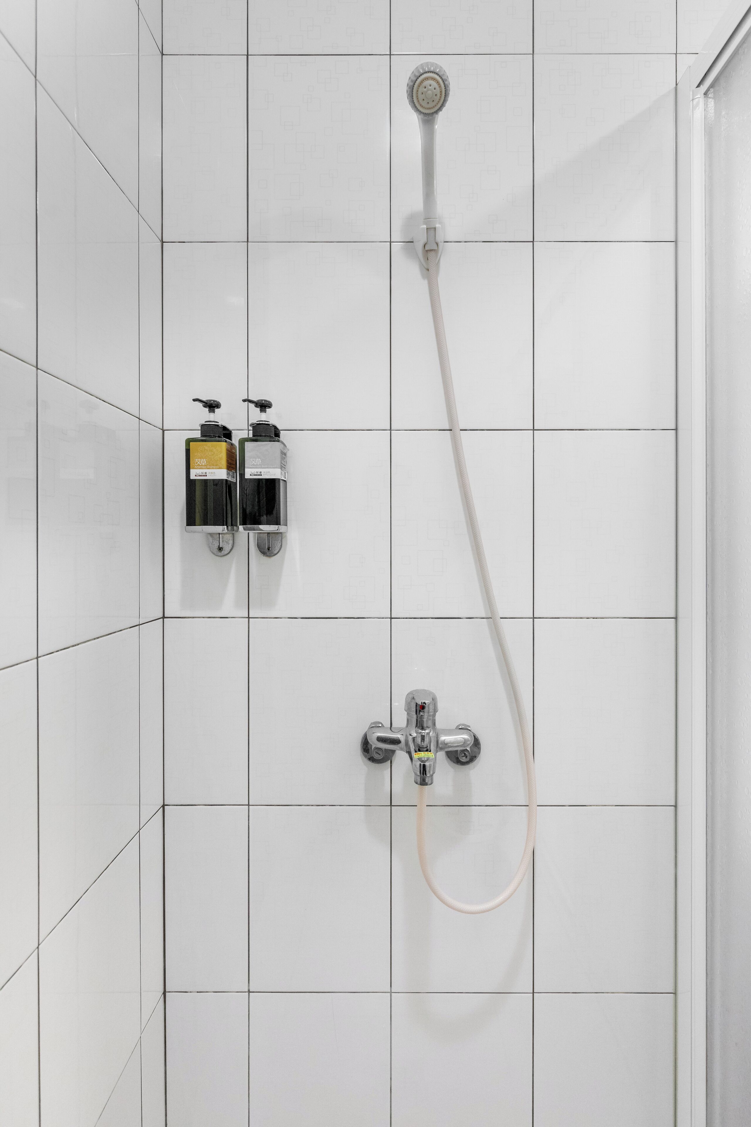 A shower with a handheld showerhead and a wall-mounted faucet. There are two soap dispensers on the wall.