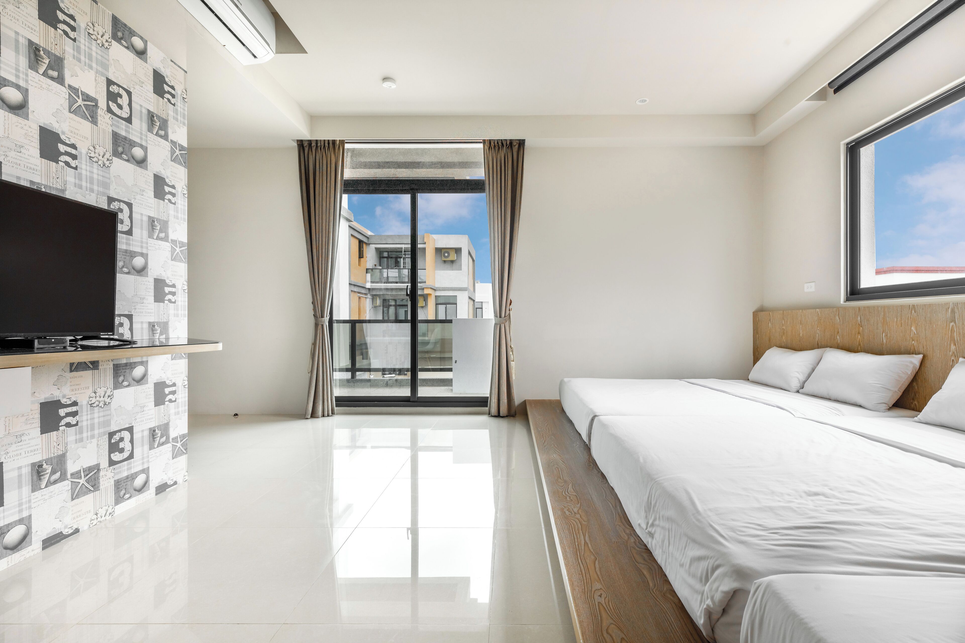 A hotel room with a large bed, a flat-screen TV, and a view of buildings through a glass door.