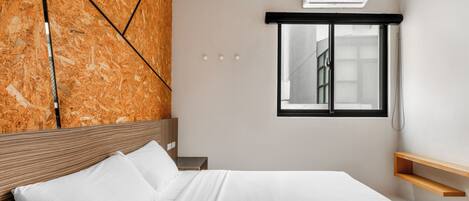 A modern bedroom with a wooden headboard, a bed with white linens, a window with a view, and a built-in air conditioning unit.
