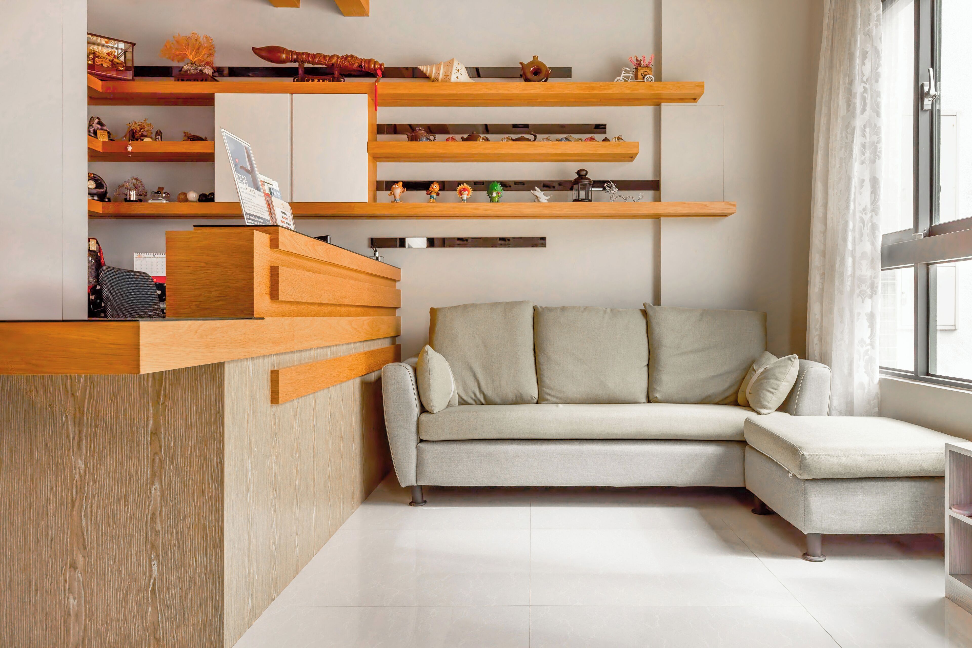 Una sala de estar moderna con un mostrador de recepción de madera, un sofá de color claro y estanterías con objetos decorativos.