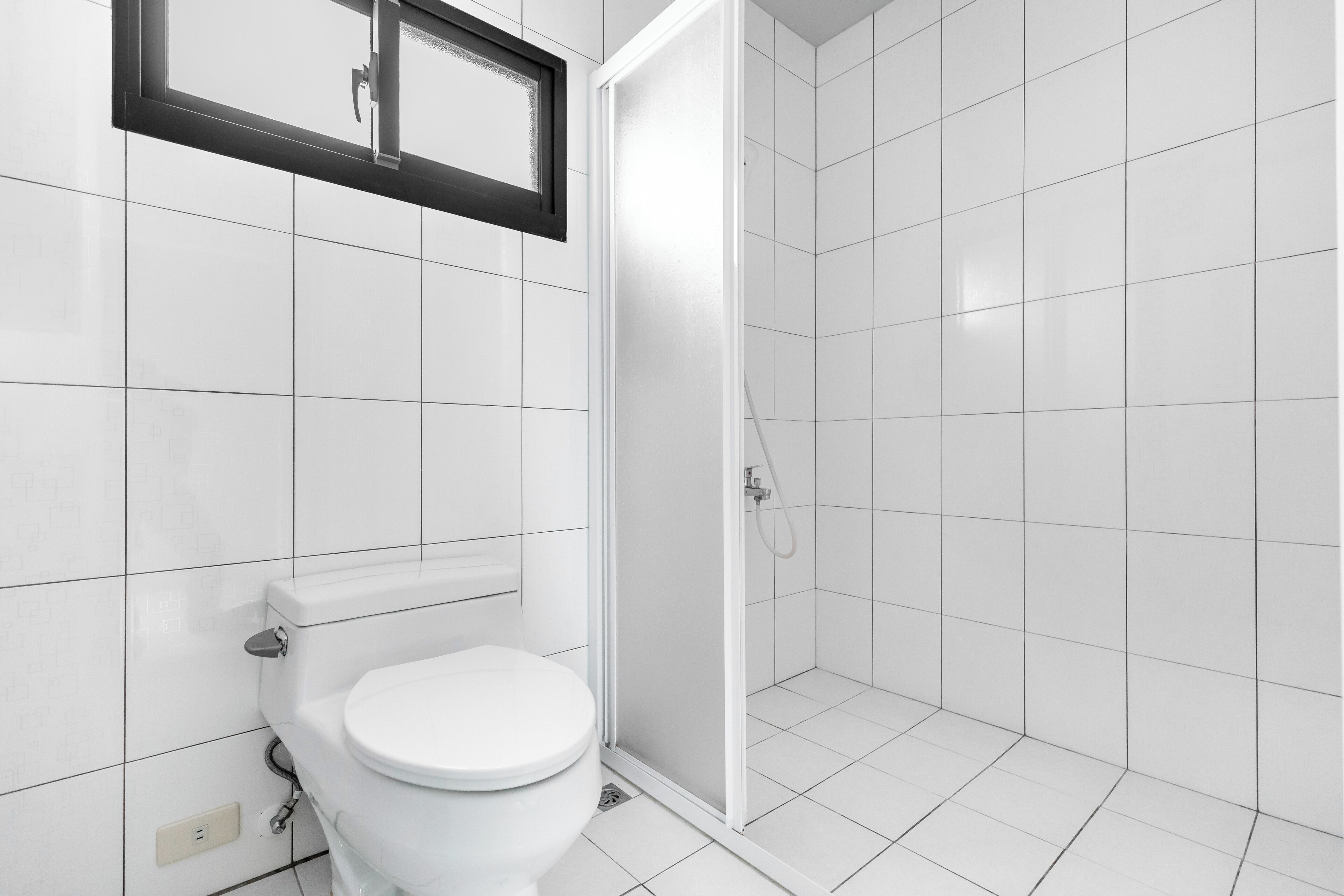 Ein modernes Badezimmer mit Toilette, Duschkabine und weißen Fliesen.