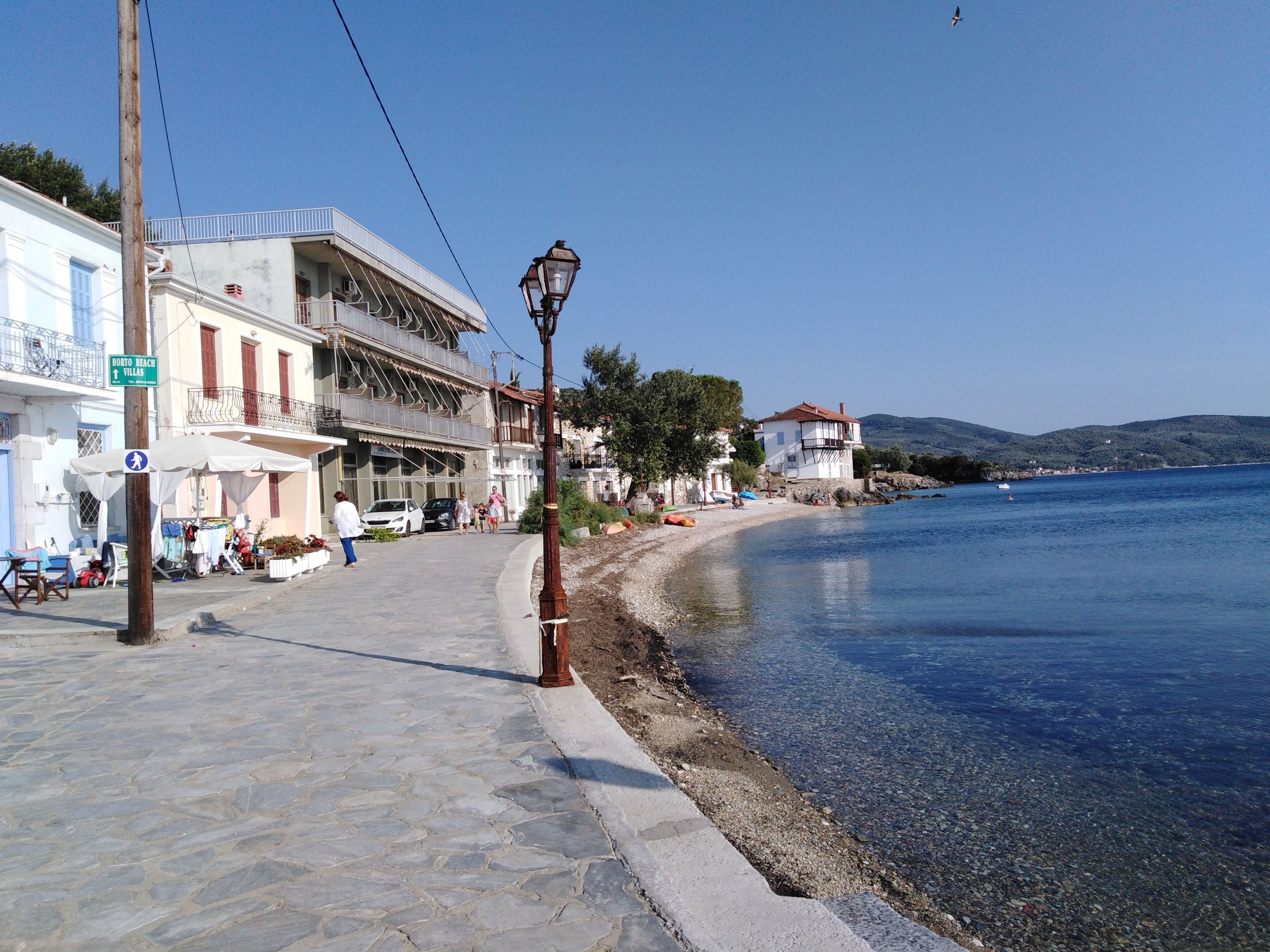 A coastal street with buildings, a clear sky, and a calm sea.