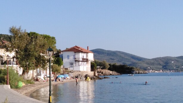 Una località costiera con un edificio bianco e un tetto rosso, una spiaggia sabbiosa e un mare calmo.