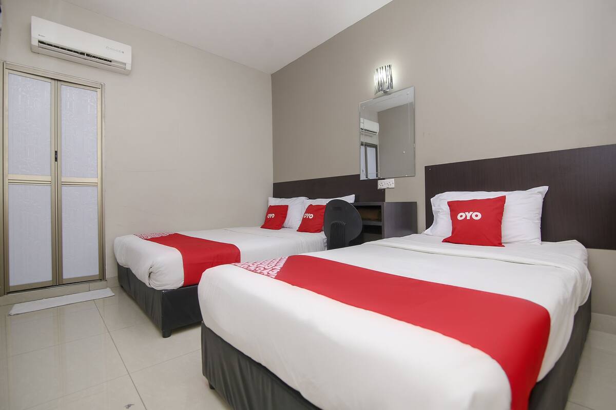 A hotel room with two beds, each with white bedding and red accents, a large mirror, and an air conditioning unit on the wall.