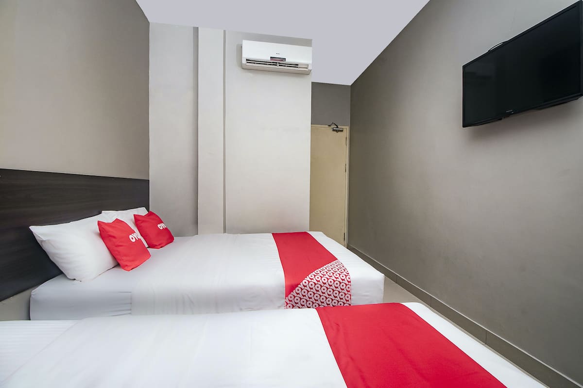 A hotel room with two beds, a TV mounted on the wall, and an air conditioning unit above the door.