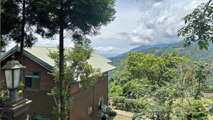 A traditional wooden house with a sloped roof, surrounded by lush greenery and a view of distant mountains. - Cloud Falls Resort (Ren'ai)
