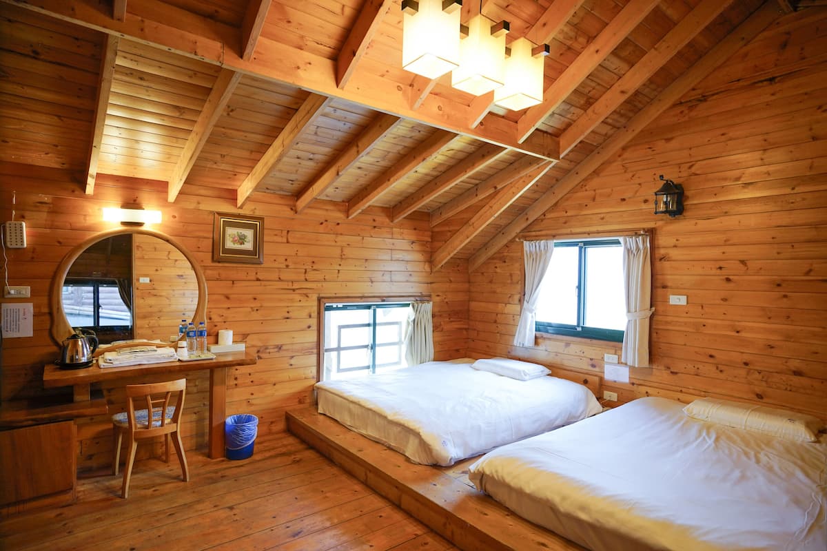 Un dormitorio de cabaña de madera con dos camas, un escritorio, una silla y una ventana.