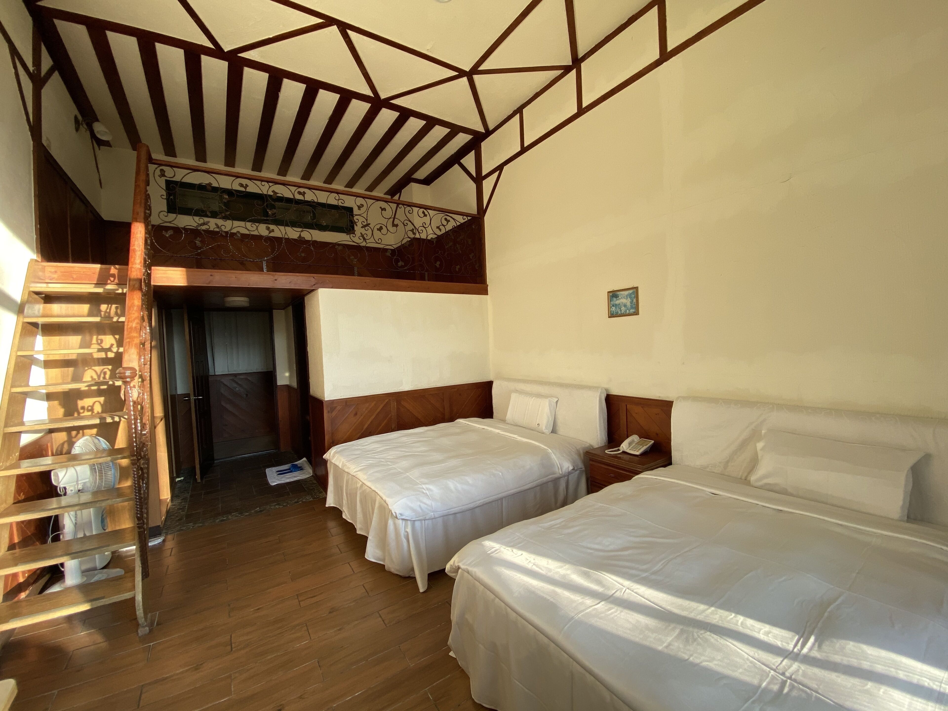 Une chambre avec deux lits, un plancher en bois, un espace de couchage en mezzanine et une petite table de chevet avec un téléphone.