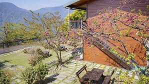 A wooden cabin with a stone patio, a wooden deck, and a view of mountains. - Cloud Falls Resort (Ren'ai)