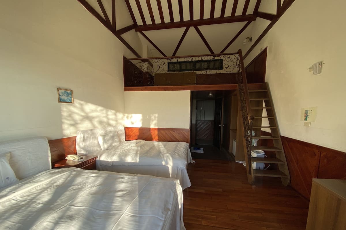 Una habitación con dos camas, una escalera de madera y una pequeña mesa de madera.