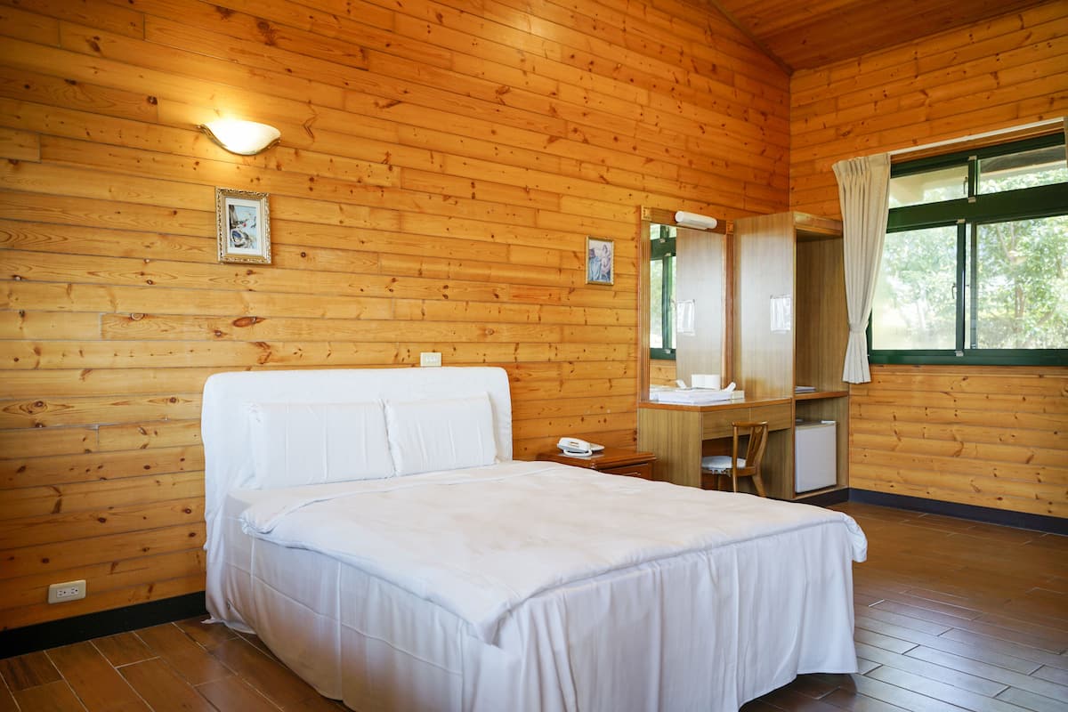 Una habitación con paneles de madera, una cama, una mesita de noche, un espejo y una ventana con cortinas.
