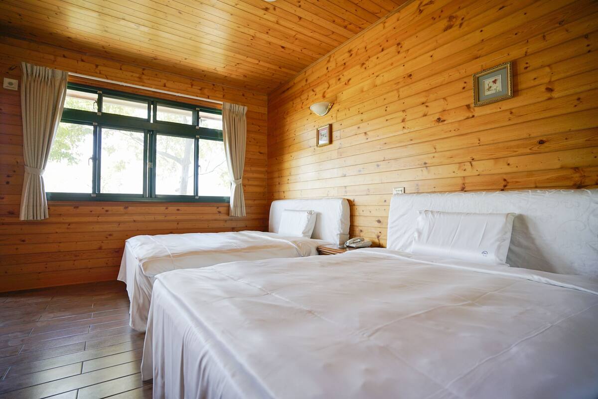 Una habitación con paredes de madera, dos camas, un ventanal con cortinas y un cuadro en la pared.