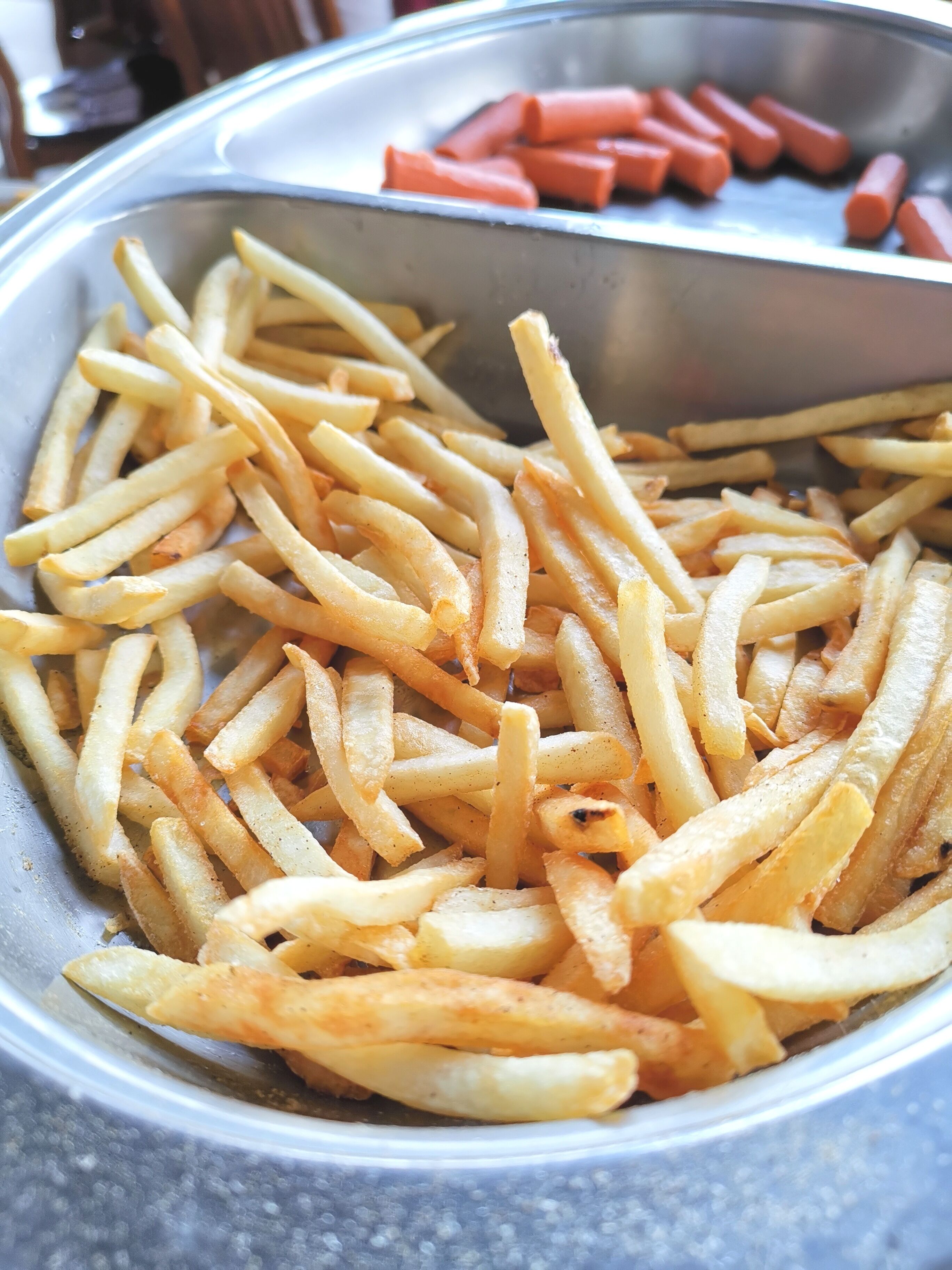 A metal bowl filled with French fries and some sausages.