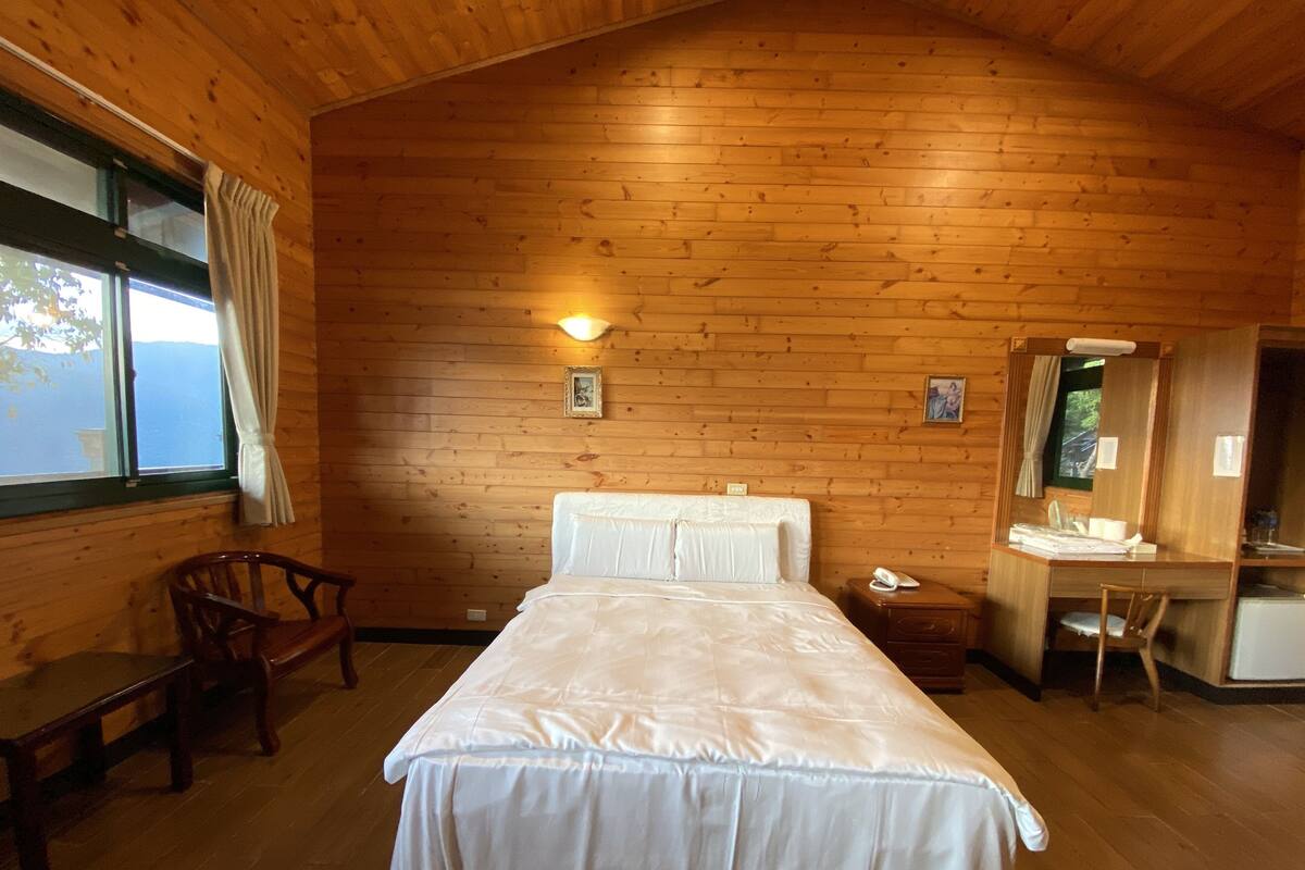 Una habitación de cabaña de madera con una cama, un escritorio, una silla y una ventana.