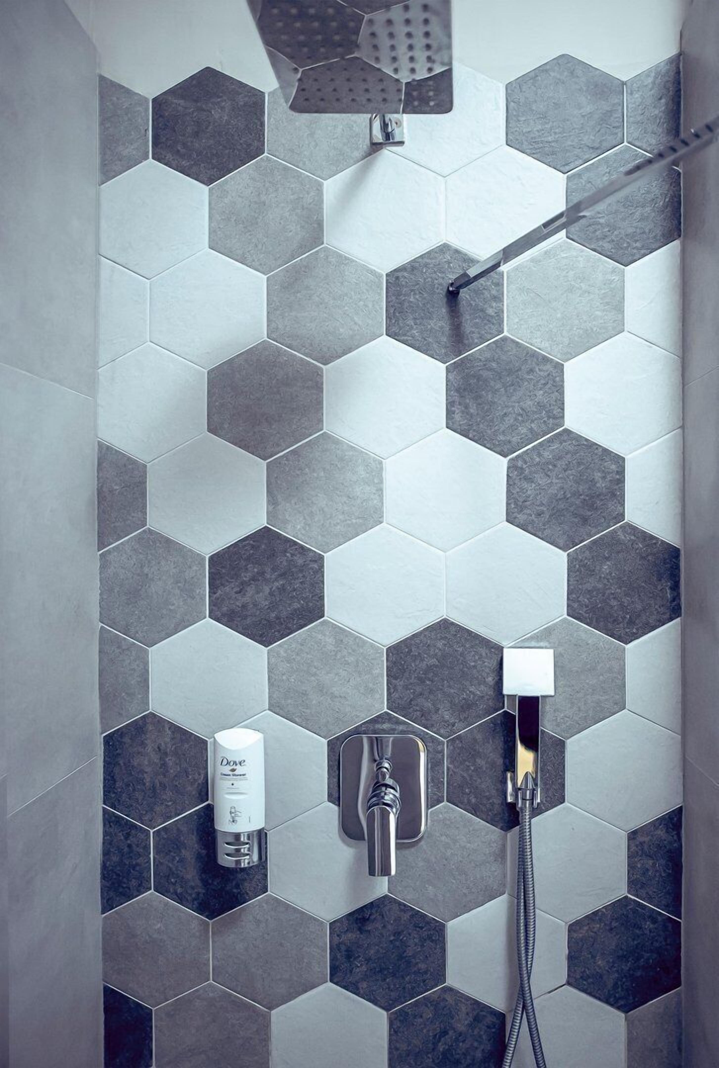 A shower area with hexagonal tiles in varying shades of gray, a handheld showerhead, and a handheld soap dispenser.