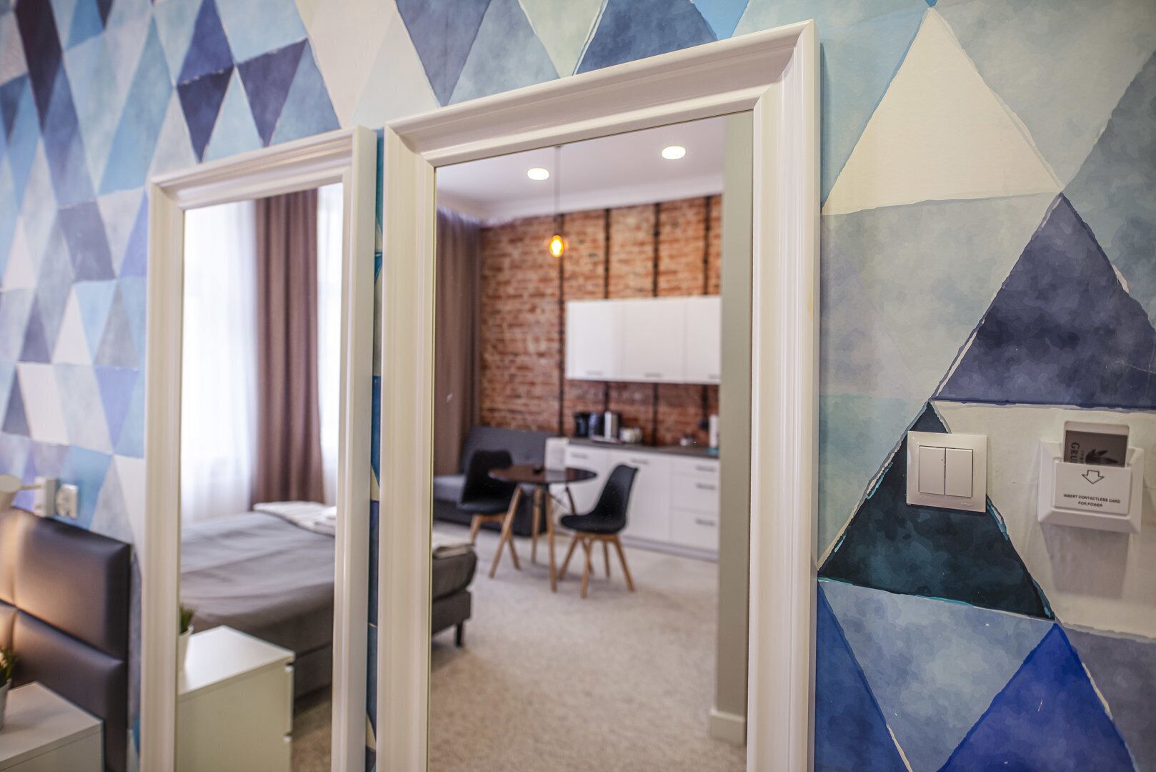 A hotel room with a bed, a desk, and a view of a dining area and kitchen.