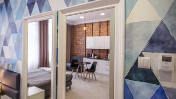 A hotel room with a bed, a desk, and a view of a dining area and kitchen.