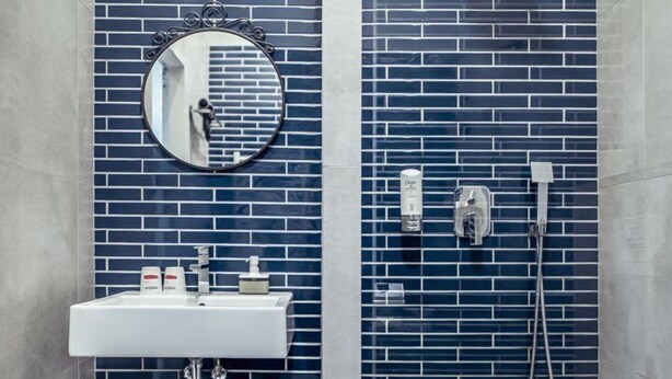 A bathroom with a white sink, a round mirror, and a shower with a blue-tiled wall.