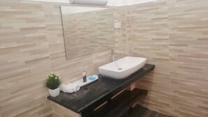 A bathroom with a white sink, a mirror, and a wooden wall. There is a small potted plant and toiletries on the counter.