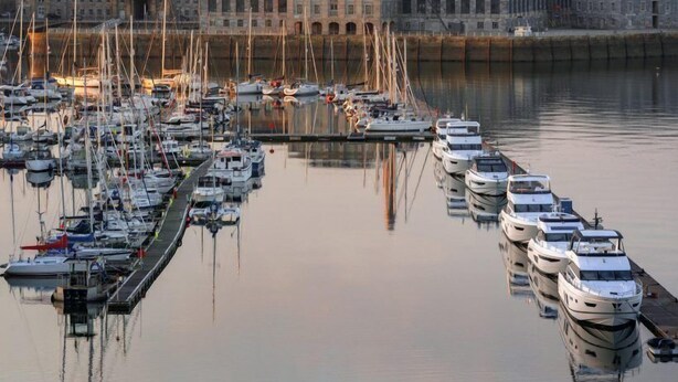 A marina with multiple boats docked, a prominent building with a tower, and a calm water body reflecting the structures. - RWY Suite48 (Plymouth)