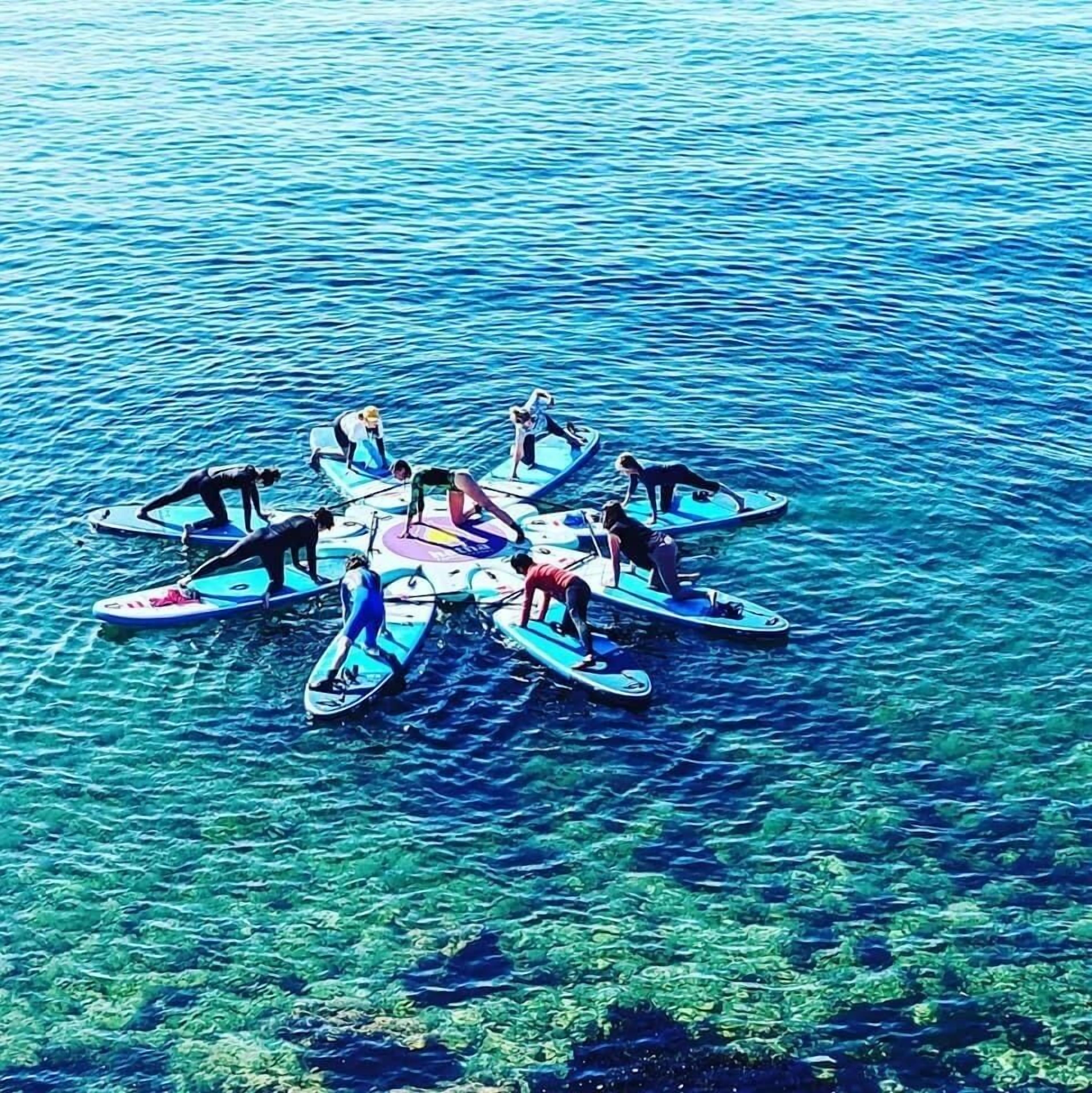 Een groep mensen op paddleboards in een cirkelvormige opstelling op het water.