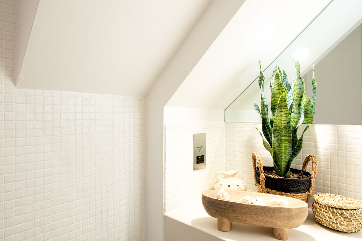 Ein modernes Badezimmer mit weißen Fliesen, einem Holzbecken, einem Blumentopf und einem Spiegel.