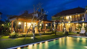 A well-lit outdoor area with a swimming pool, a covered seating area, and a building with multiple balconies. - The Runik Ubud (Ubud)
