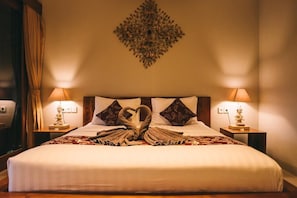 Un letto rifatto con cura, un asciugamano a forma di cuore, due lampade sui comodini e un elemento decorativo a parete.