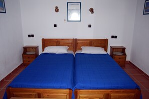 Una cama doble con ropa de cama azul, cabecera de madera, dos mesitas de noche y un cuadro enmarcado en la pared.