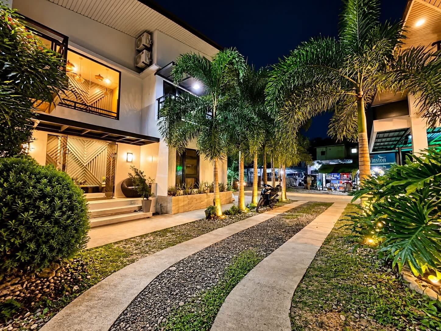 A modern building with a well-lit entrance, a paved pathway, and surrounding greenery.