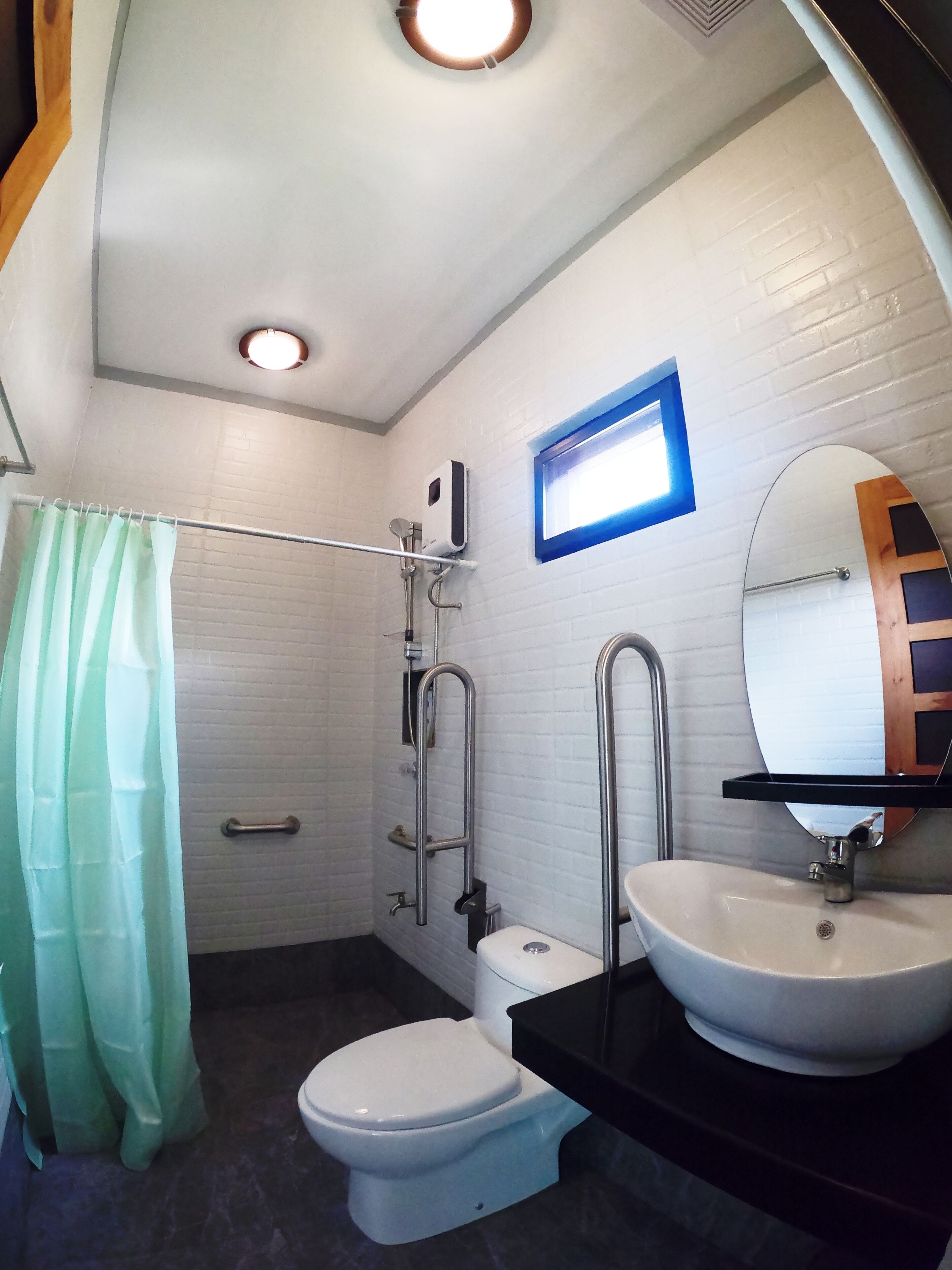 A modern bathroom with a white toilet, a sink with a mirror, a shower with a handheld showerhead, and a green shower curtain.