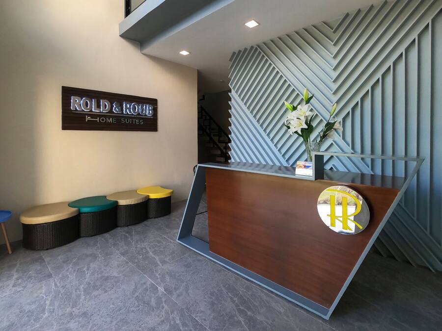 Un área de recepción con un cartel que dice "ROLD & HOME SUITES" y un moderno mostrador de recepción con un logotipo.