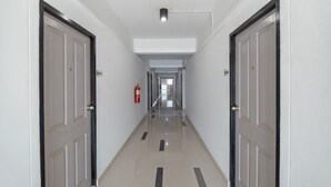 A corridor with doors on both sides, a fire extinguisher on the left wall, and a ceiling light fixture.