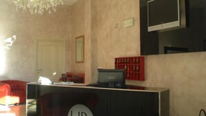 A hotel reception area with a desk, a television, a chandelier, and a red seating area.