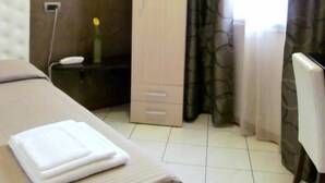A hotel room with a bed, a wardrobe, a desk with a lamp, and a chair.