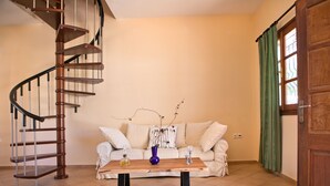 A living room with a spiral staircase, a sofa set, a coffee table, and a door with a green curtain. - Hot Tub Cottage Kalymnos (Kalymnos)
