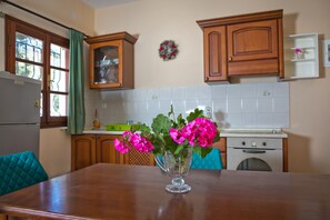 A kitchen with wooden cabinets, a white tiled backsplash, a dining table with a clear glass vase of flowers, and a refrigerator.