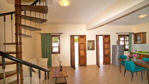 A spacious living area with a wooden staircase, a dining table with chairs, and a kitchen area with cabinets. - Hot Tub Cottage Kalymnos (Kalymnos)