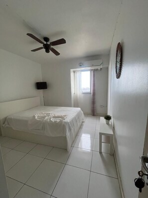 A bedroom with a bed, a ceiling fan, a window with curtains, and a wall-mounted air conditioner.