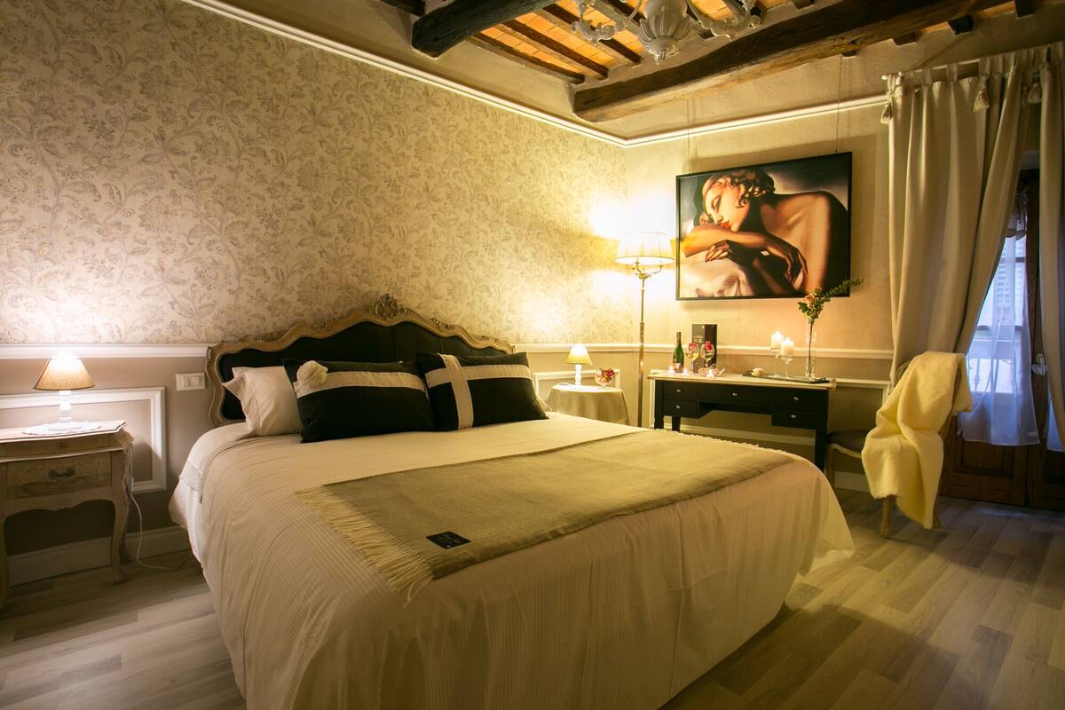 A well-appointed hotel room with a large bed, a desk, a chair, and a painting on the wall.