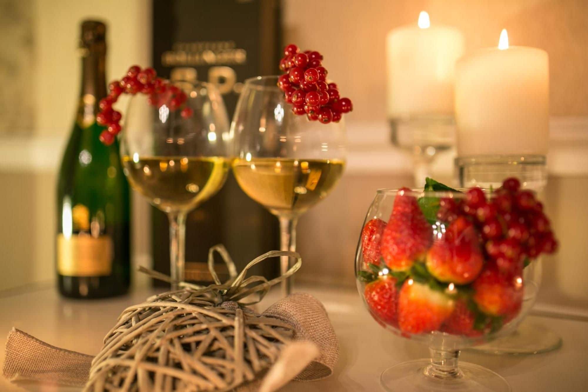Una mesa dispuesta con una botella de vino, dos copas de vino, una vela y un frutero.