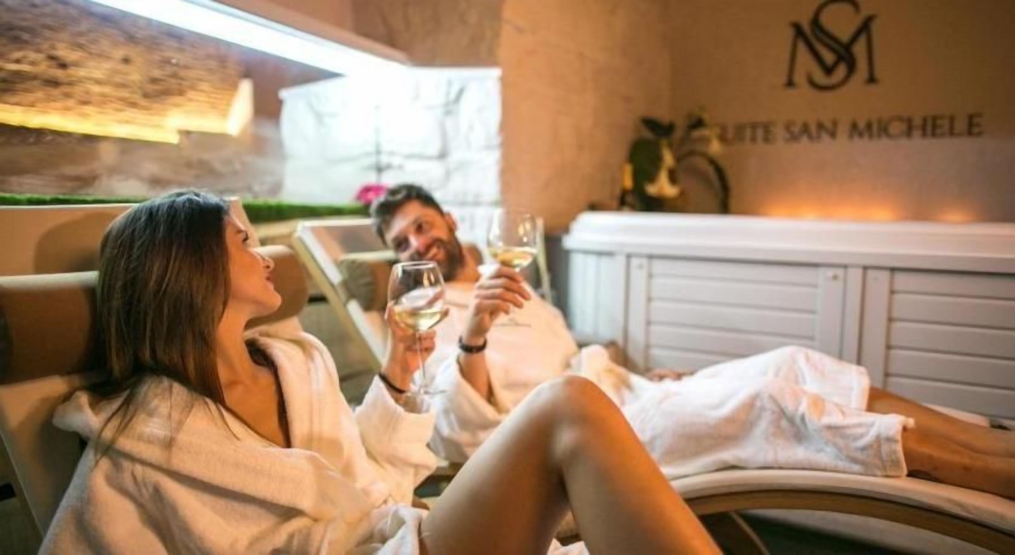 Una pareja se relaja en un spa con un logotipo visible en la pared, un mostrador de recepción y una planta al fondo.