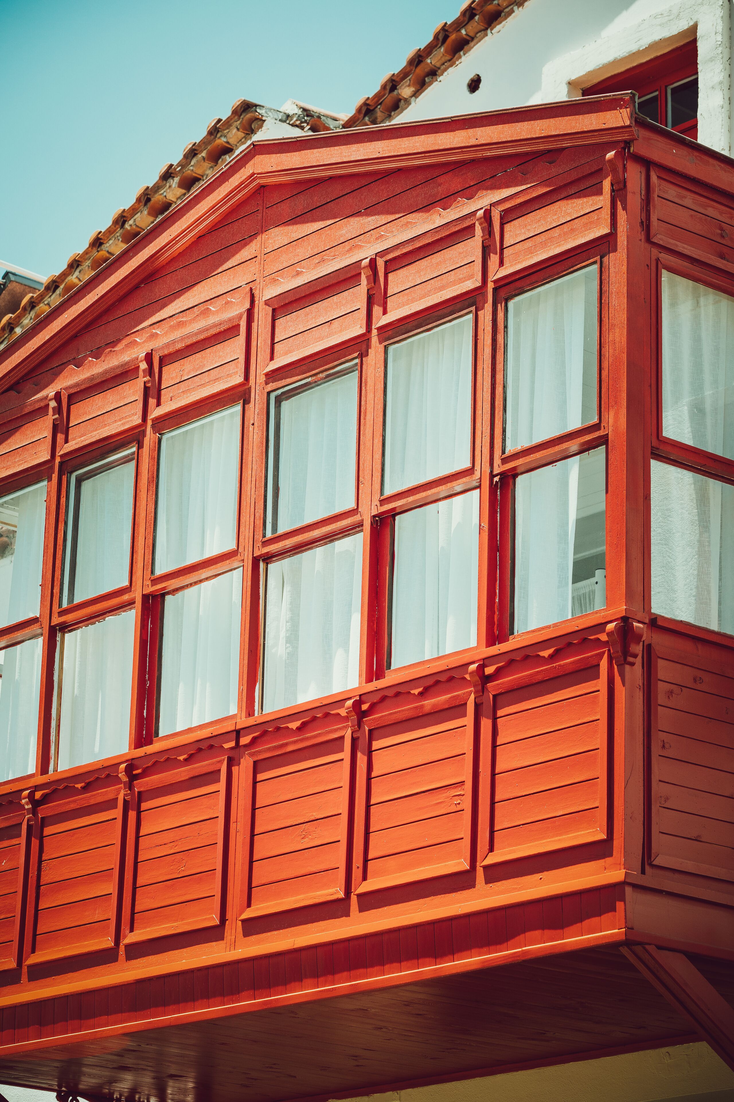 A red wooden balcony with multiple windows and a white wall.