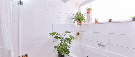 A modern bathroom with white tiled walls, a freestanding bathtub, and various potted plants.