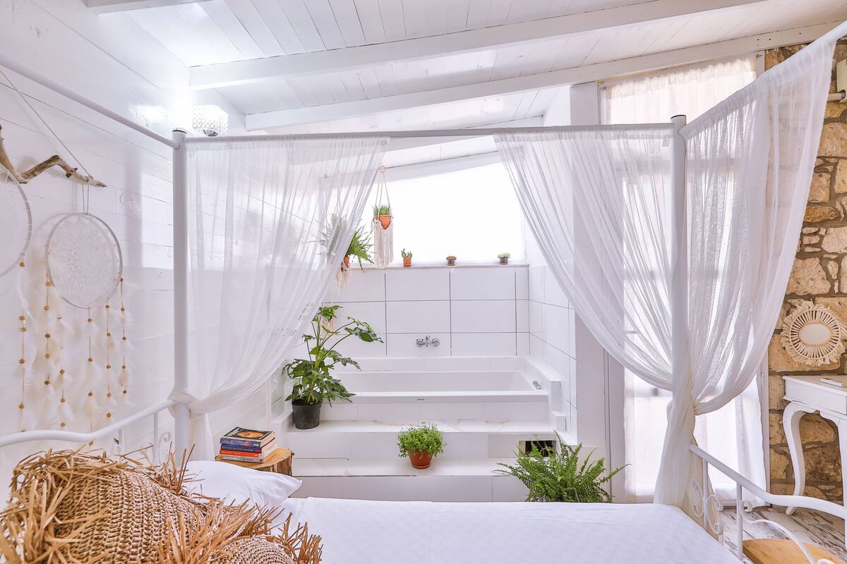 A white bathroom with a bathtub, a vanity, and a window with sheer curtains.