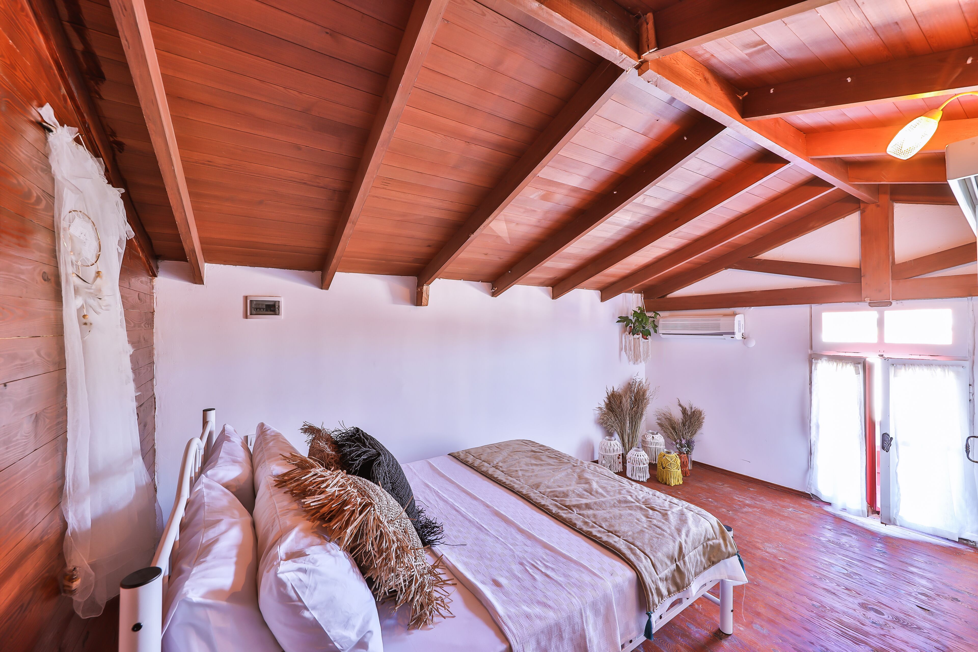 Ein Schlafzimmer mit Holzboden, einem Bett mit vielen Kissen, einem Nachttisch und einem Fenster mit Vorhängen.