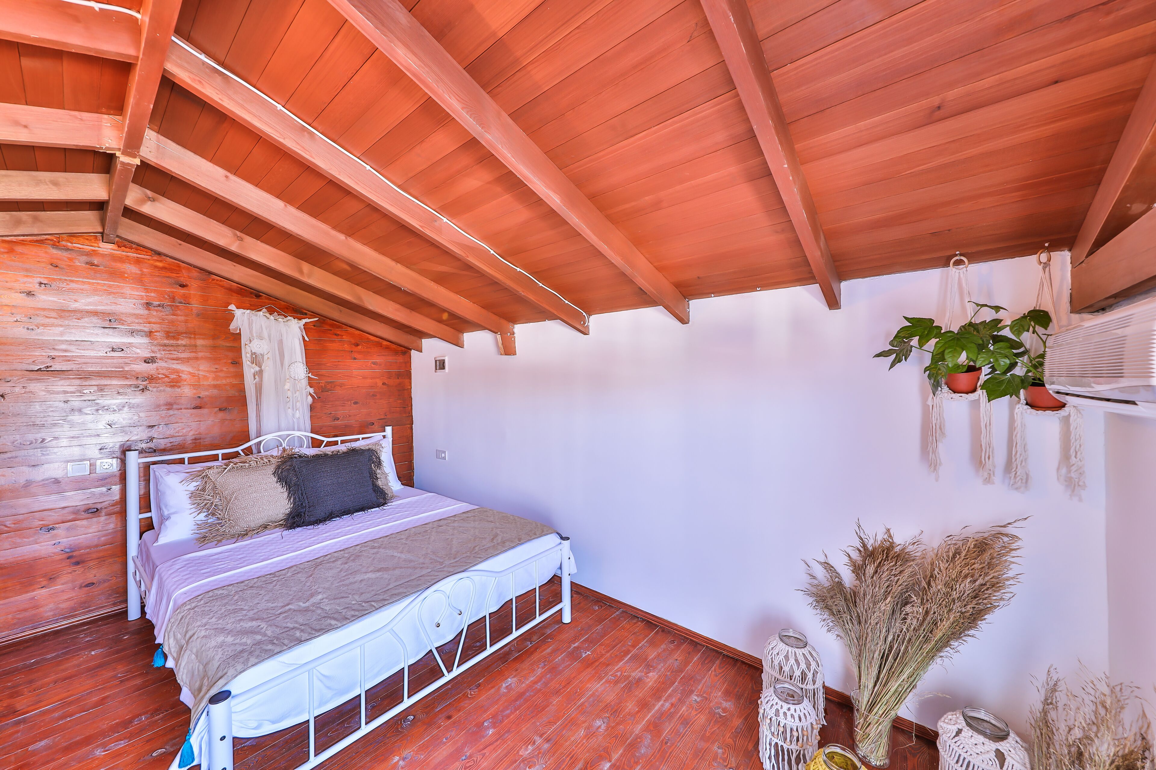 A bedroom with a wooden ceiling, a white metal bed frame, and a white wall.