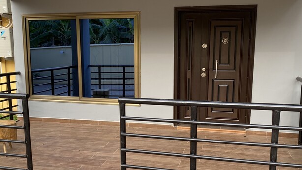 A view of a house's exterior, including a gated entrance, a window with a view of greenery, and a door with a modern design. - 3-bed Apartment, Sleeps 6 With Wi-fi (Sakumono)