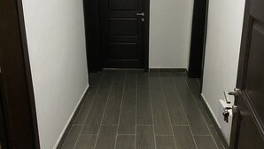 A hallway with dark wooden flooring and white walls, leading to a black door with a handle. - 3-bed Apartment, Sleeps 6 With Wi-fi (Sakumono)