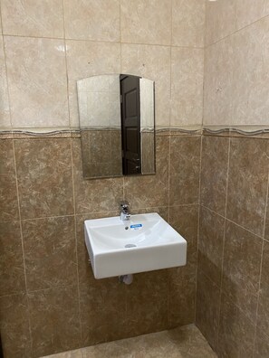 A bathroom with a white sink, a mirror, and brown tiled walls. - 3-bed Apartment, Sleeps 6 With Wi-fi (Sakumono)